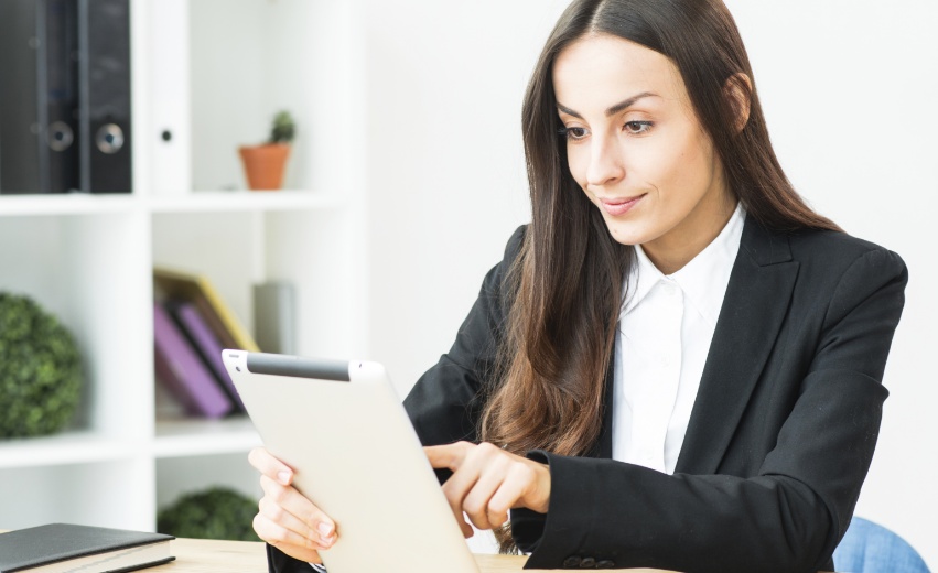 Mulher branca de terno observa e toca em um tablet