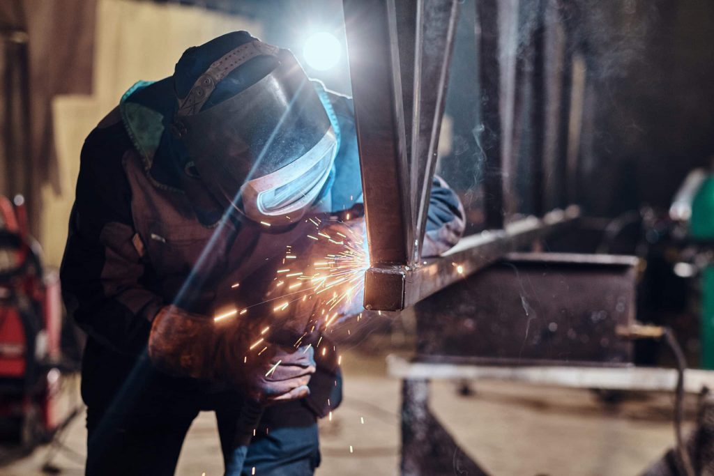 Foto de um soldador exercendo sua atividade com mascará de ferro.