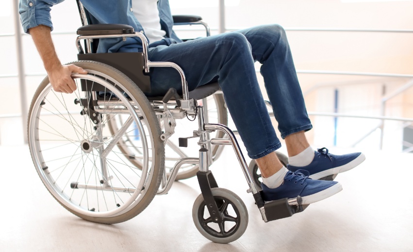 A foto mostra uma pessoa do peito para baixo utilizando uma cadeira de rodas
