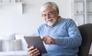 Homem branco idoso sorri enquanto observa um tablet