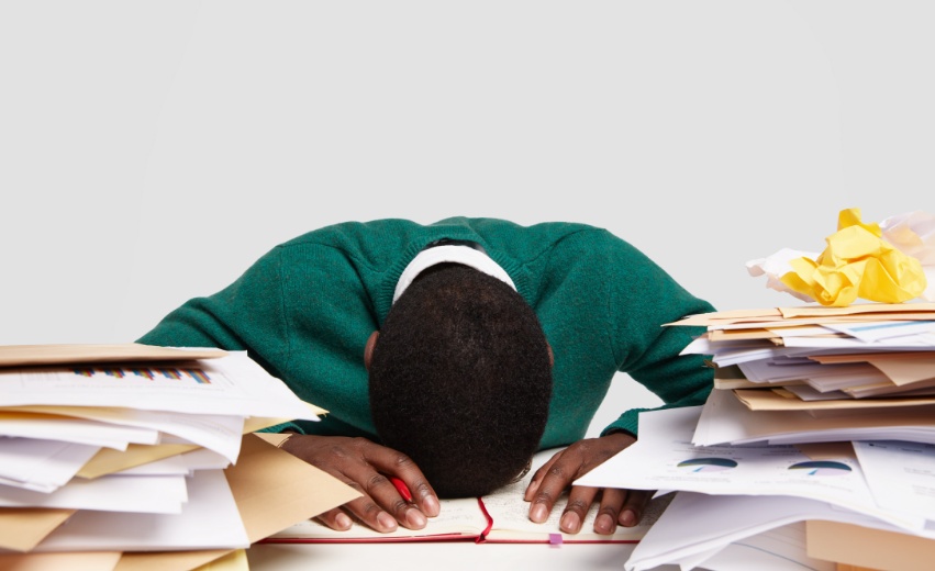 Trabalhador negro exausto e com a cabeça encostada em uma mesa cheia de papéis.