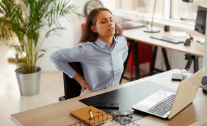 Mulher em frente a mesa de trabalho sente dor nas costas.