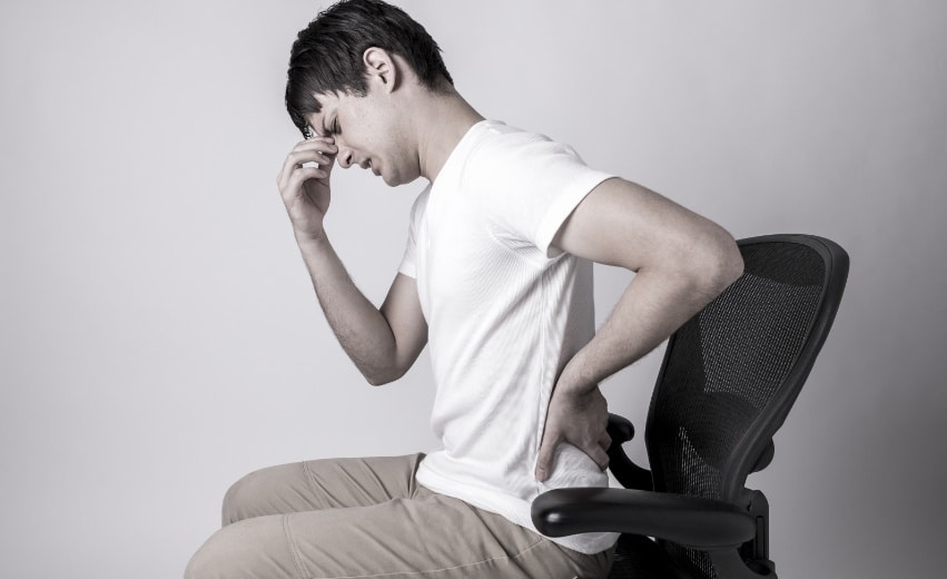 Homem sentando em cadeira sente fortes dores nas costa em razão da espondilite anquilosante.