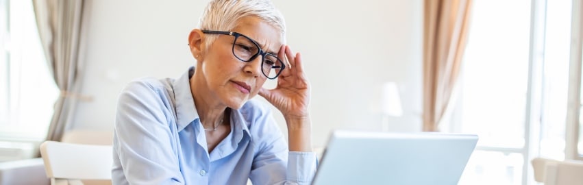 Mulher branca idosa com semblante de preocupação e olhando para uma telade computador