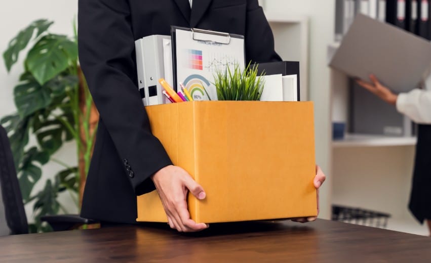 Mãos de mulher carregando uma caixa de papelão simbolizando uma demissão