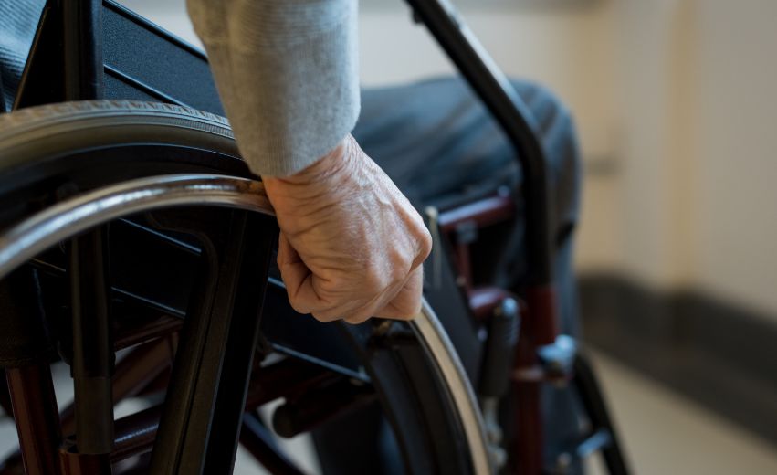 Mão idosa segurando a roda de uma cadeira de rodas.