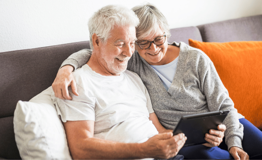 Dois idosos sorridentes observando um tablet.