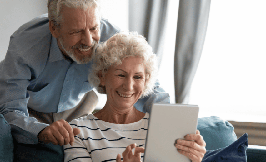 casal de idosos sorridentes olhando para um tablet.