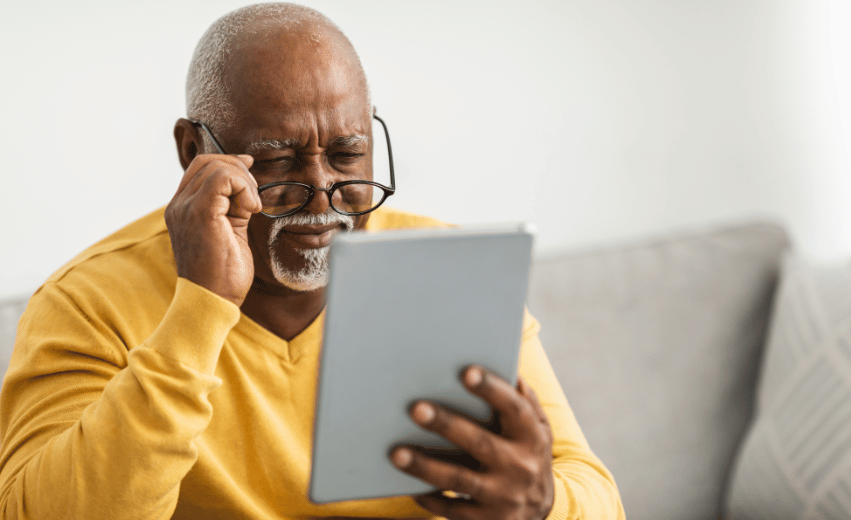 Homem idosos negro sentado em um sofa com um tablet btranco na mão calculando o RMI do INSS.
