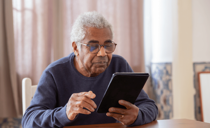 Homem idoso negro sentado em um sofá com um tablet analisando qual a melhor regra de transição para aposentadoria.