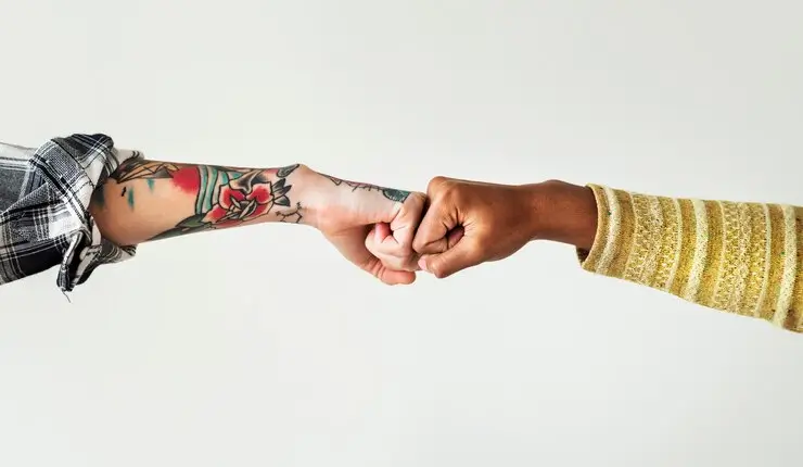 Um homem tatuado e uma mulher negra juntam as mãos.